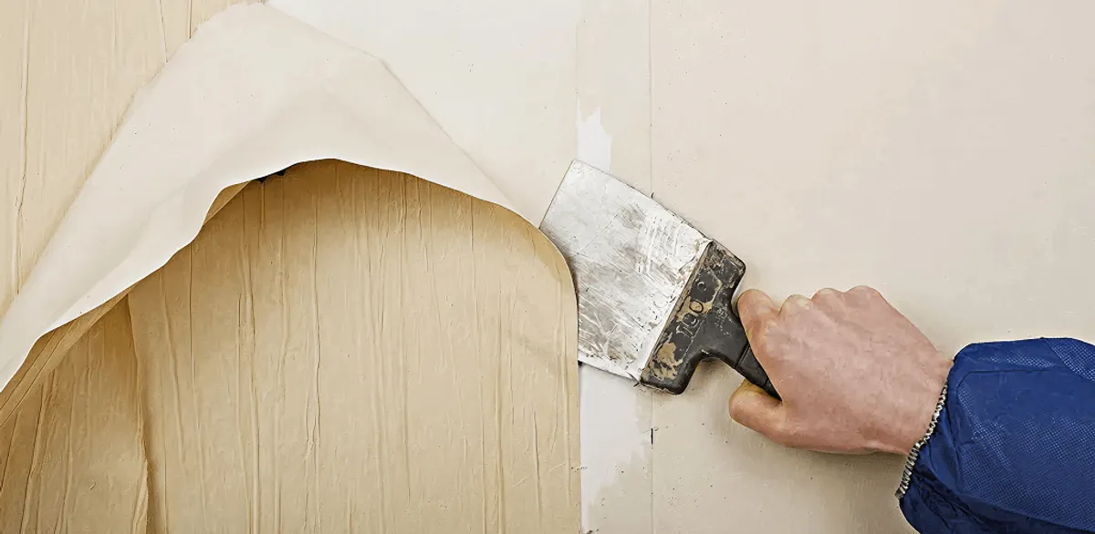 Handyman removing wallpaper with a scraper for wall preparation in Seattle, WA