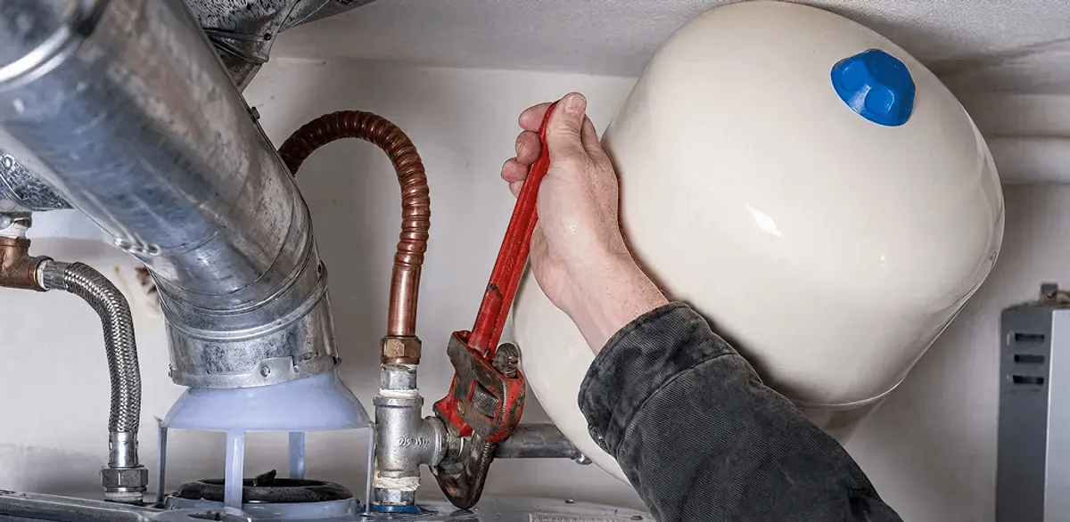 Water heater repair technician tightening plumbing connections near a tank unit in Seattle, WA